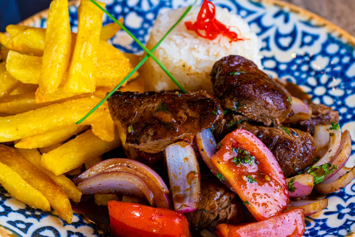 A plate of Peruvian lomo saltado with beef, onion, tomato, fries and rice, representative of criollo cooking